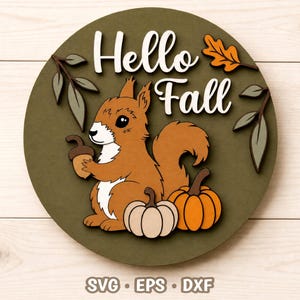 Op de afbeelding: Een rond olijfgroen houten bord met de witte tekst Hello Fall. Het ontwerp bevat een bruine eekhoorn die een eikel vasthoudt, een lichtbeige pompoen, een oranje pompoen en decoratieve takken in tinten groen en oranje.