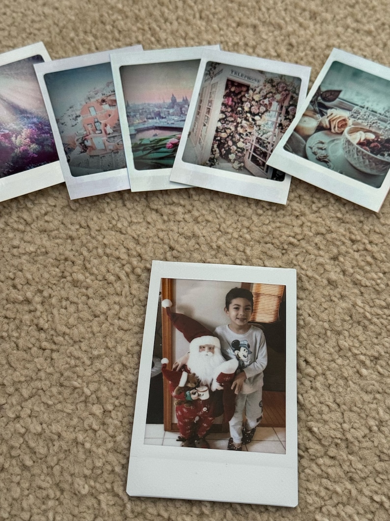 May include: A Polaroid photo of a young person standing next to a Santa Claus figure. The person is wearing a light blue shirt with a Mickey Mouse design and white pants. The Santa Claus figure is wearing a red and white suit with a white beard.