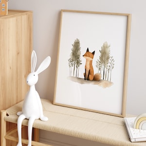 May include: A watercolor print of a fox sitting in a forest with trees behind it. The print is framed in a light wood frame and is hanging on a wall.