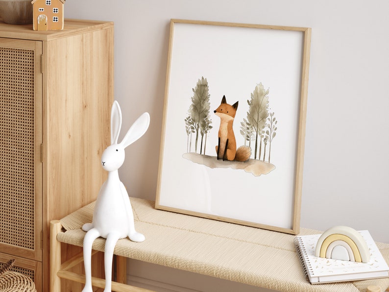 May include: A watercolor print of a fox sitting in a forest with trees behind it. The print is framed in a light wood frame and is hanging on a wall.