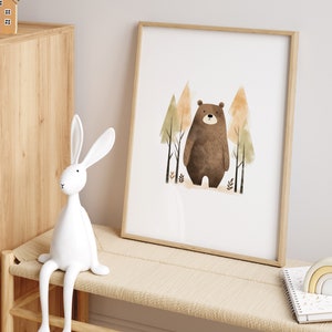 May include: A framed print of a brown bear standing in a forest with green and orange trees. The print is in a light wood frame and is hanging on a white wall.