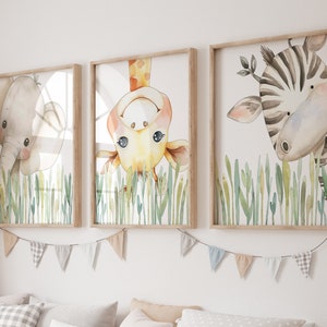 May include: Three framed watercolor paintings of animals peeking out from behind green grass. The paintings feature a giraffe, an elephant, and a zebra.