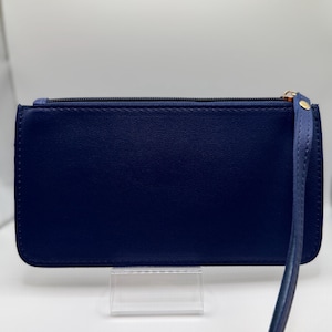 Pu&ograve; includere: Una pochette blu navy con cinturino da polso. Il portafoglio rettangolare ha una chiusura a cerniera e un tirazip dorato. Il cinturino da polso &egrave; attaccato al lato con un rivetto dorato.