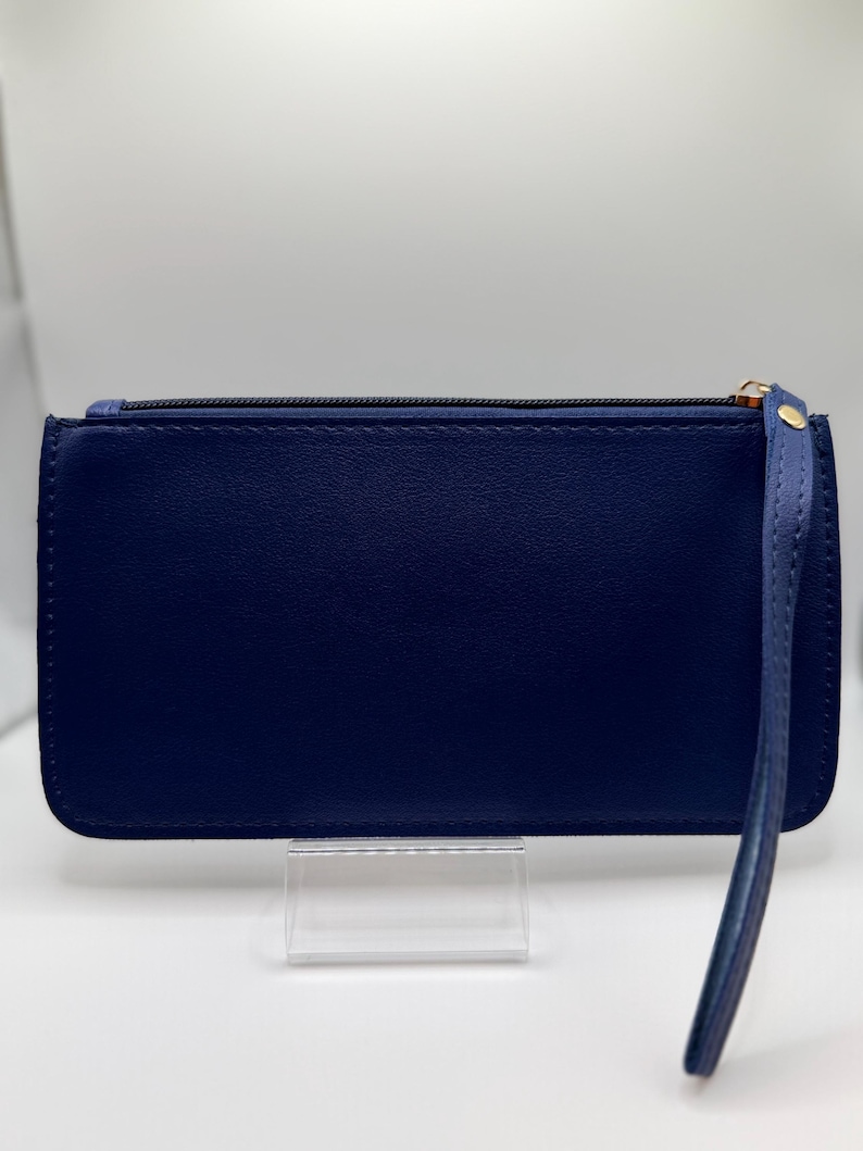 Pu&ograve; includere: Una pochette blu navy con cinturino da polso. Il portafoglio rettangolare ha una chiusura a cerniera e un tirazip dorato. Il cinturino da polso &egrave; attaccato al lato con un rivetto dorato.