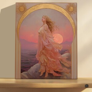 May include: A framed art print featuring a woman in a flowing gown standing on a rocky shore. The artwork has a warm color palette with shades of pink, peach, and gold. The background depicts a sunset over the ocean.