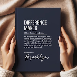 May include: A navy blue notebook with the words "DIFFERENCE MAKER" in white. The definition of "Difference Maker" is printed below the title. The name "Brooklyn" is written in cursive at the bottom of the page.