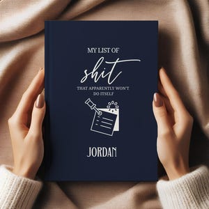 May include: A navy blue notebook with the text "MY LIST OF shit THAT APPARENTLY WON'T DO ITSELF" and the name "JORDAN" in white. The notebook features a humorous illustration of a pushpin and a notepad.