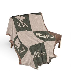 May include: A woven blanket with a checkerboard pattern in green and beige. The blanket features the letters "RN" with a caduceus symbol, a graduation cap, the year "2016", and the name "Mira" in white script. The edges have a fringed trim.
