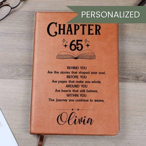 May include: A personalized brown leather journal with the text "CHAPTER 65" and the name "Olivia". The journal includes inspirational text about life's journey. The word "PERSONALIZED" is at the top. A bookmark is visible.