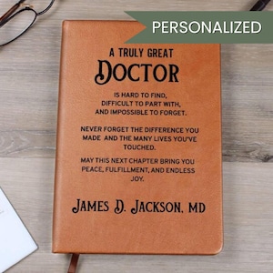 Può includere: Un diario personalizzato in pelle marrone con il testo "A Truly Great Doctor" e un messaggio. Il diario include il nome "James D. Jackson, MD". Un segnalibro è visibile.