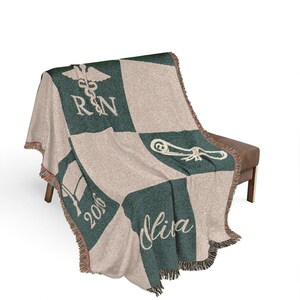 May include: A woven blanket with a green and beige checkered pattern. The blanket features the caduceus symbol, the letters "RN", a graduation cap, the year "2016", and the name "Mira" in white script. The blanket has a fringed edge.