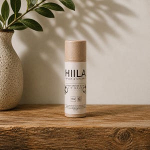 Könnte beinhalten: Eine zylindrische Papphülse mit Hiila veganem und biologischem Lippenbalsam mit süßer Orange und Limette. Das Etikett zeigt schwarzen Text auf cremefarbenem Hintergrund, inklusive Markenname, Produktart und einem Nettogewicht von 11g.