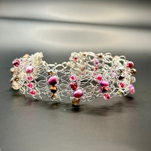 May include: A silver wire bracelet with pink and clear beads woven into the design.