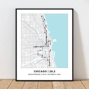 May include: A framed map print of Chicago featuring a black line route overlay on a gray street grid with a light blue lake section. The text at the bottom reads CHICAGO | 26.2, MAGGIE BESKON | 4:14:47 | OCTOBER X, XXXX in black sans-serif font.