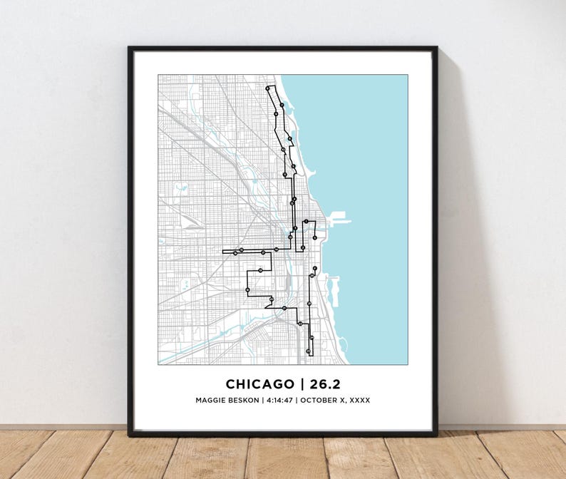 May include: A framed map print of Chicago featuring a black line route overlay on a gray street grid with a light blue lake section. The text at the bottom reads CHICAGO | 26.2, MAGGIE BESKON | 4:14:47 | OCTOBER X, XXXX in black sans-serif font.