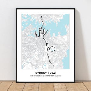 May include: Framed print featuring a black line map of Sydney, Australia, with a light blue water background. The text "SYDNEY | 26.2" is at the bottom, along with the runner's name, time, and date. The print is in a black frame.