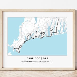 May include: Framed print featuring a map of Cape Cod with a black line tracing a 26.2-mile route. The map is set against a light blue background. Text at the bottom reads "CAPE COD | 26.2" with a name, time, and date.