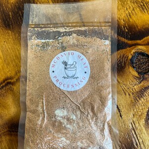 May include: A clear plastic bag containing a brown spice blend. The bag has a white label with the text "McDavid Meat Processing" in black.