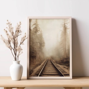 Op de afbeelding: Een ingelijste sepia-kleurige foto van een spoorweg die verdwijnt in een mistig bos. Het spoor is gemaakt van hout en metaal, en het bos is dicht met hoge bomen.