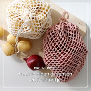 Op de afbeelding: Twee gebreide netten voor groenten en fruit, een witte en een roze, op een houten oppervlak met aardappelen en een rode biet. De tekst "GROENE DIY KIT haak je eigen groenten en fruit netje" is zichtbaar op de afbeelding.