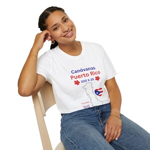 Puede incluir: Camiseta blanca con el texto "Canóvanas Puerto Rico" en azul y rojo, un contorno de mapa y la bandera de Puerto Rico. La camiseta también presenta el texto "100 X 35" y un diseño floral.