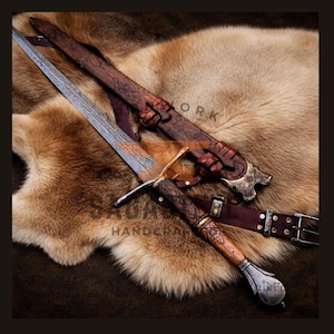May include: A handcrafted sword with a detailed blade and wooden handle, resting on a fur pelt. The sword is accompanied by a brown leather sheath and belt. The image includes the text "Saga Handcraft".