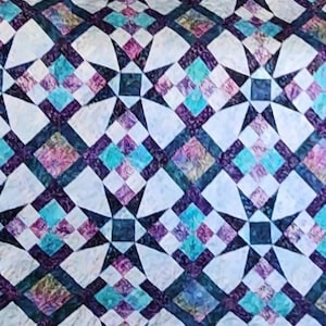 Puede incluir: Una colcha con un patrón geométrico de estrellas y diamantes en tonos azules, morados y blancos.