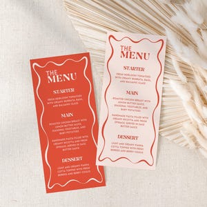 May include: Two red menu cards with white text and a decorative border. The cards list a starter, main course, and dessert. The menu is displayed on a neutral background with dried floral accents.