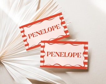 May include: Two rectangular cards with the name "PENELOPE" in red letters. The cards have a light pink background with a red border and red stripes. The cards are placed on a white, textured background.