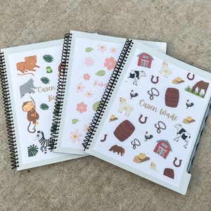May include: Three spiral bound notebooks with different themes. The first notebook has a jungle theme with animals like a monkey, zebra, elephant, and leopard. The second notebook has a floral theme with pink flowers and green leaves. The third notebook has a farm theme with animals like cows, horses, chickens, and a red barn. The text on the third notebook says "Casen Wade".
