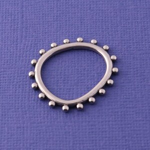 May include: A silver-toned ring featuring a thin, circular band adorned with a series of small, evenly spaced spherical beads along the outer edge, creating a textured, dotted appearance around the entire circumference of the jewelry piece.