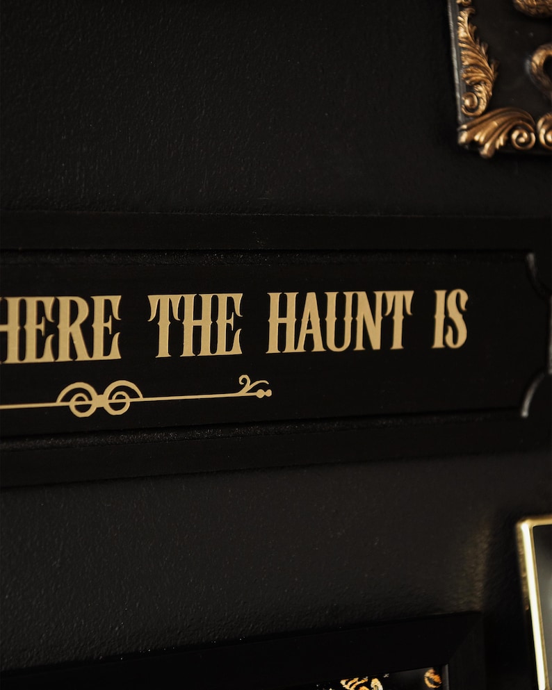 May include: Black sign with gold lettering that reads "Where the haunt is".