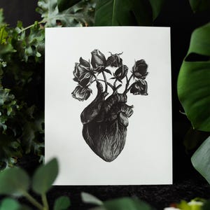 A black and white print of a hand-drawn anatomical heart blooming with wilted roses as though it were a vase. Surrounded by dark green leaves and shadows. Ideal for gothic or anatomy-themed decor.