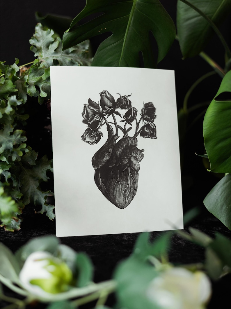A black and white print of a hand-drawn anatomical heart blooming with wilted roses as though it were a vase. Surrounded by dark green leaves and shadows. Ideal for gothic or anatomy-themed decor.