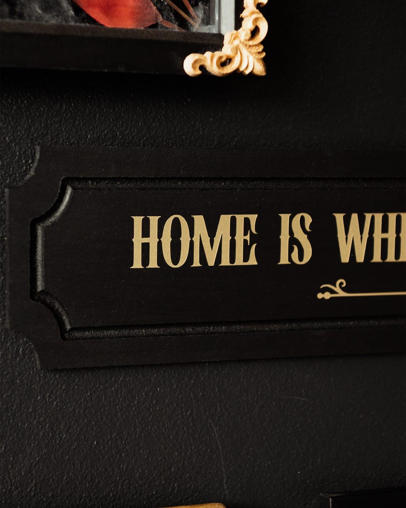 May include: Black wooden sign with gold lettering that reads "HOME IS WHERE THE HEART IS".