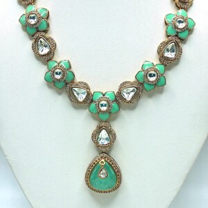 May include: A gold-toned necklace featuring a floral design with mint green enamel petals and clear, faceted gemstones. The necklace has a central pendant with a teardrop-shaped, mint green stone, surrounded by smaller clear stones.