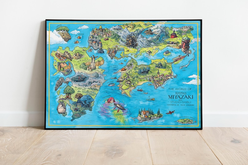 May include: A framed, colourful map illustration titled "The World of Hayao Miyazaki Studio Ghibli." The map features a detailed, whimsical depiction of a fantasy world with various landmarks, characters, and a blue ocean.