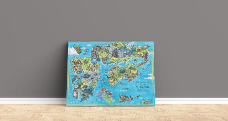 May include: A framed, illustrated map of a fantasy world, leaning against a grey wall. The map is filled with colorful landscapes and characters. Text on the map reads "The World of Hayao Miyazaki Studios Ghibli".