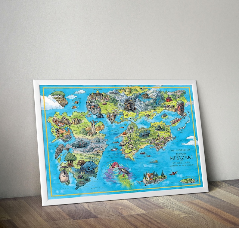 May include: A framed art print showing a detailed, illustrated map of a fantasy world. The map includes various locations and characters, with the text "THE WORLD OF HAYAO MIYAZAKI STUDIO GHIBLI". The frame is white, and the artwork is displayed on a wooden surface.