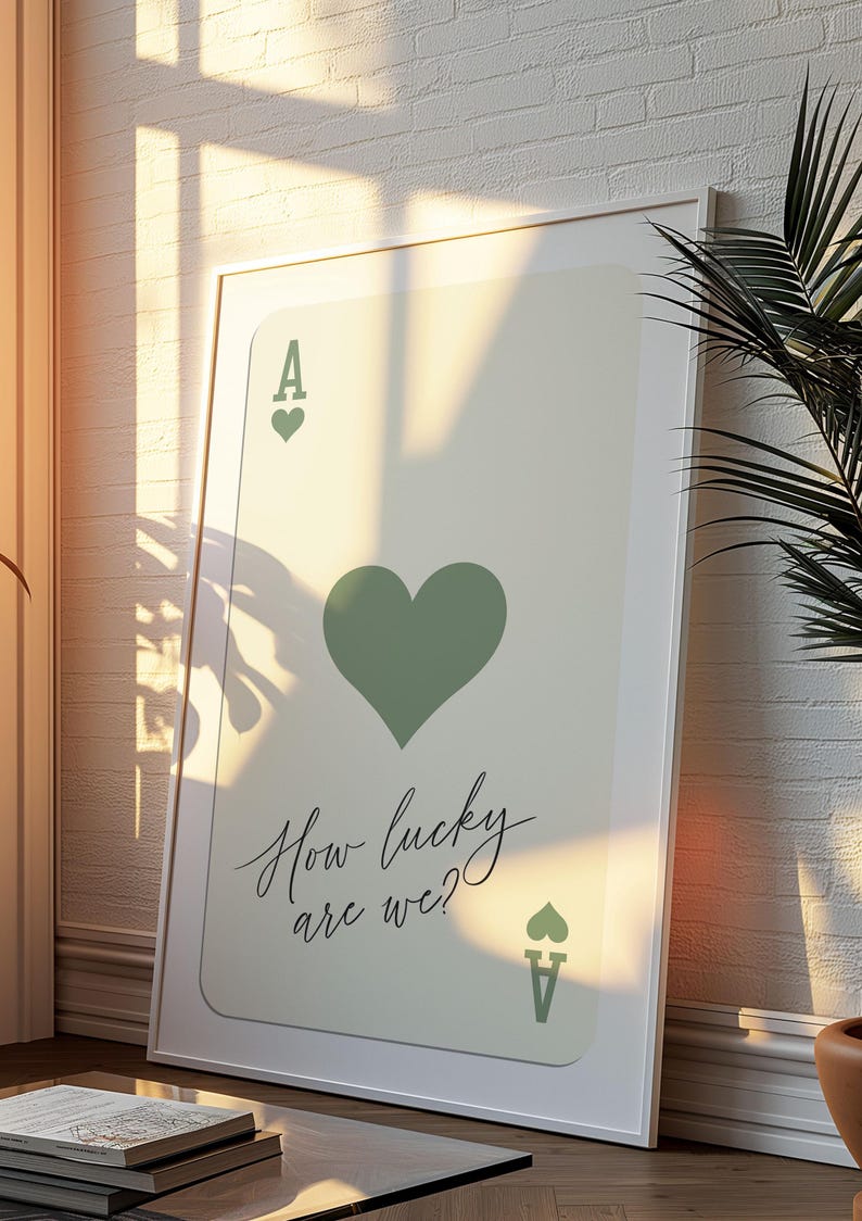 May include: A white framed print of an ace of hearts playing card with a green heart and the text "How lucky are we?"