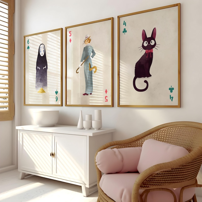 May include: Three framed art prints featuring illustrations of characters on playing card backgrounds. The prints have gold frames and are displayed on a white wall. The art includes a black cat, a figure in a blue suit, and a faceless figure.