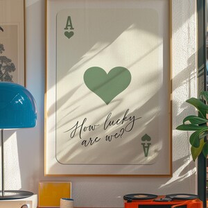 May include: A framed print of an ace of hearts playing card with a green heart and the text "How lucky are we?" printed on it.
