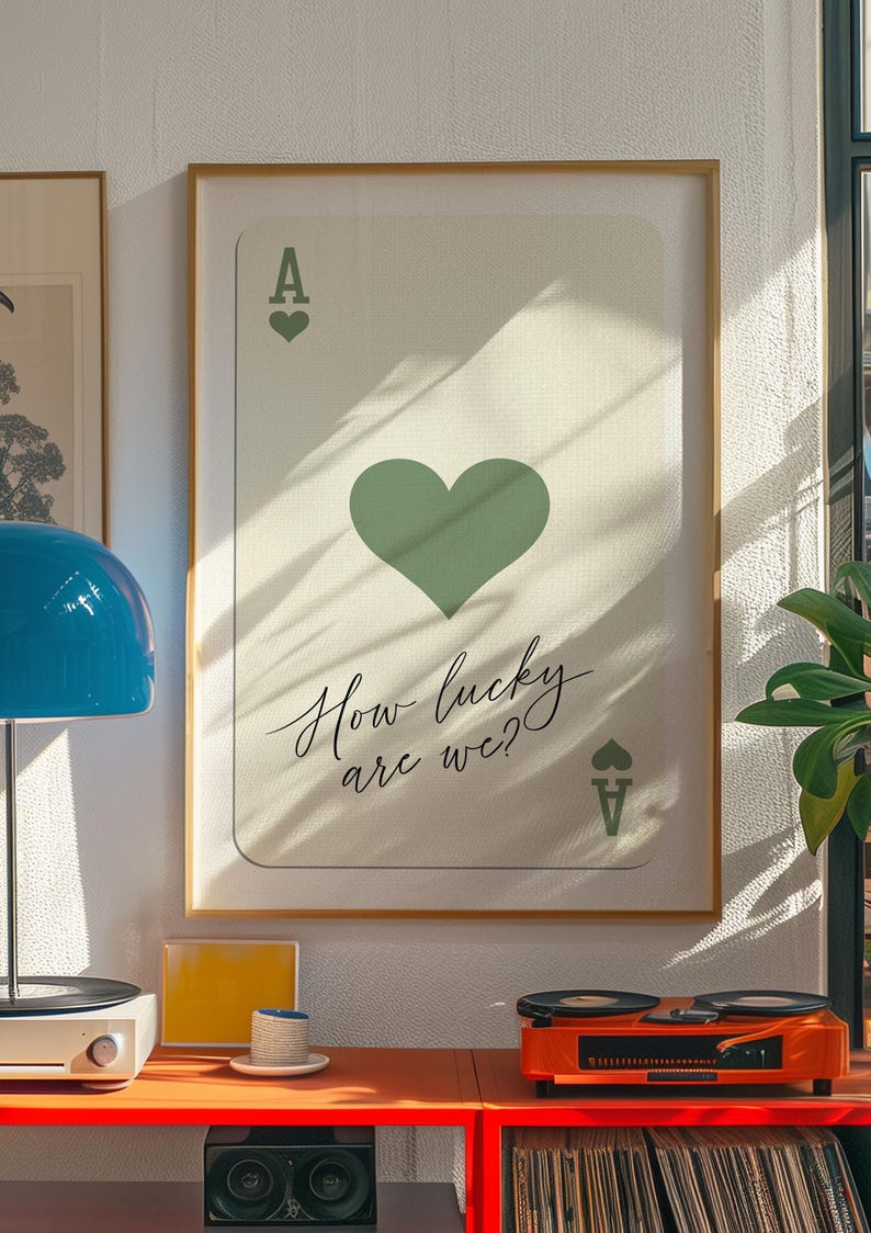 May include: A framed print of an ace of hearts playing card with a green heart and the text "How lucky are we?" printed on it.