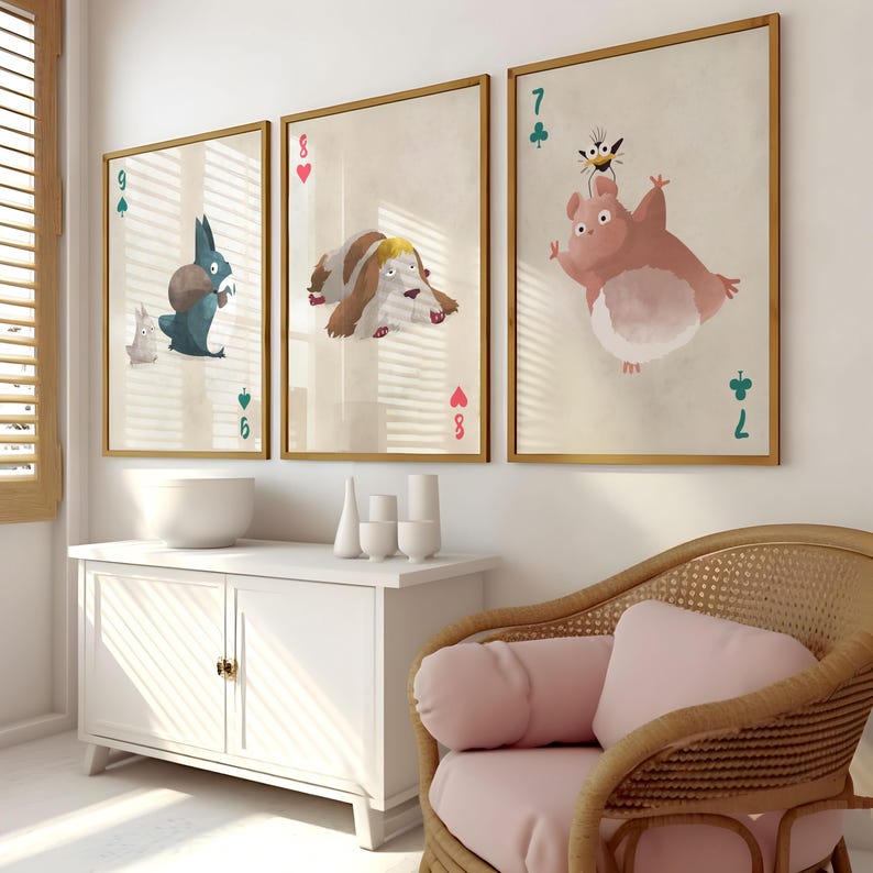 May include: Three framed prints of cartoon animals with playing card numbers and suits. The prints are on a white wall above a white cabinet and a wicker chair with a pink cushion.