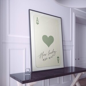 May include: A framed print of an ace of hearts playing card with a green heart and the text "How lucky are we?"