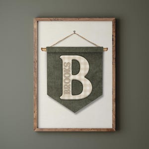 May include: A framed wall banner with a green background and a large, off-white letter "B" in the center. The letter has a plaid pattern. The word "BROOKS" is printed vertically on the left side of the banner. The banner is suspended by a rope.