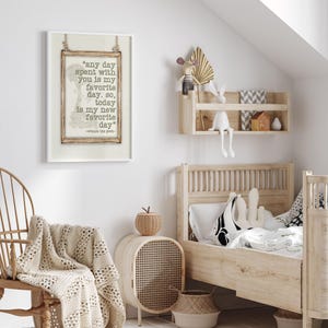 May include: A framed print featuring a quote from Winnie the Pooh: "any day spent with you is my favorite day." The print is displayed in a child's bedroom, alongside a wooden bed, a woven chair, and a decorative shelf with toys.