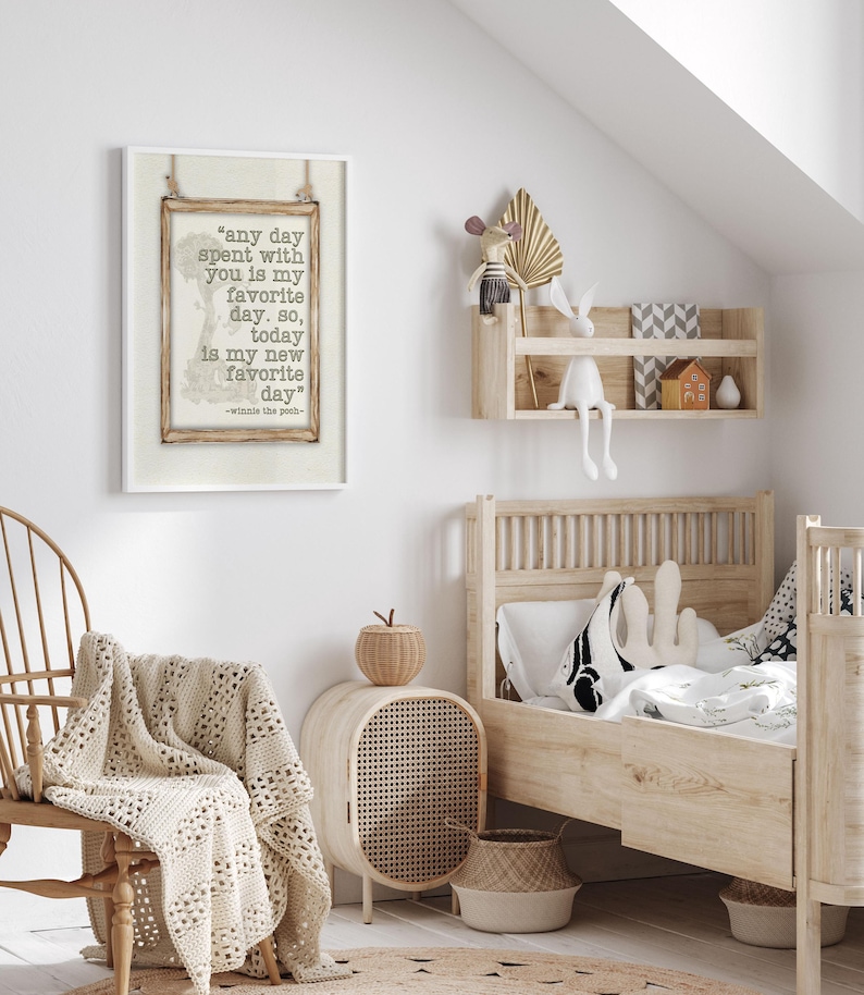 May include: A framed print featuring a quote from Winnie the Pooh: "any day spent with you is my favorite day." The print is displayed in a child's bedroom, alongside a wooden bed, a woven chair, and a decorative shelf with toys.