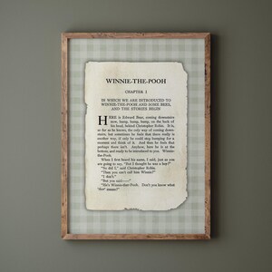 May include: A framed print of a page from "Winnie-the-Pooh." The text is displayed on a vintage paper background, with the title, chapter number, and the opening lines of the story. The frame is a light brown colour.