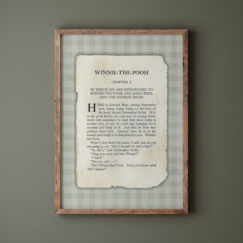 May include: A framed print of a page from "Winnie-the-Pooh." The text is displayed on a vintage paper background, with the title, chapter number, and the opening lines of the story. The frame is a light brown colour.